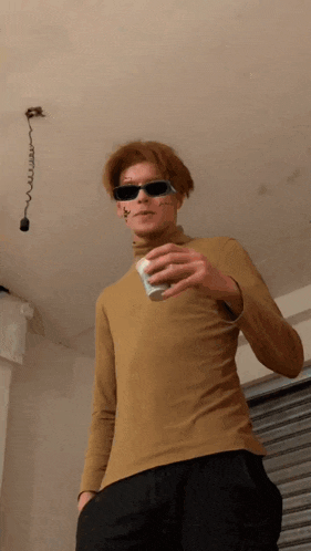a young man wearing sunglasses and a turtleneck holds a cup