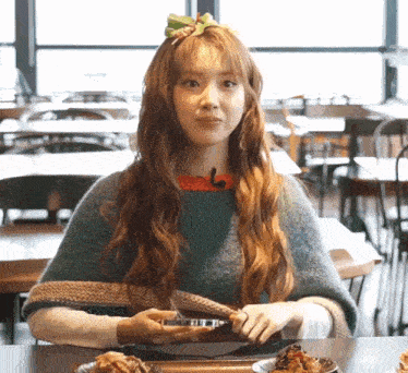 a woman with long hair is sitting at a table with a plate of food in front of her