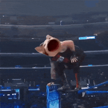 a man is laying on the ground in a wrestling ring while a dog with a big mouth is standing over him .