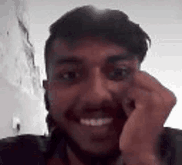 a man with a beard is smiling and making a funny face while holding his hand to his face .