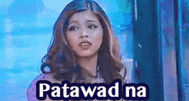 a woman is standing in front of a window with the words patawad na written on the bottom of her face .