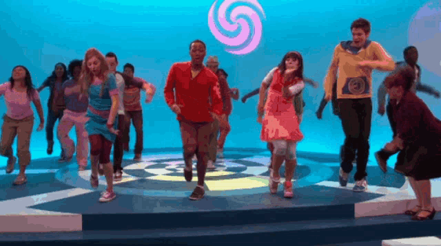 a group of people are dancing in front of a blue background with a pink swirl