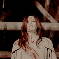 a woman with blood on her face is standing in front of a wooden structure .