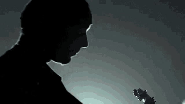 a silhouette of a man playing an electric guitar in a dark room