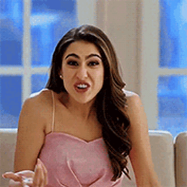 a woman in a pink top is sitting on a couch making a funny face .