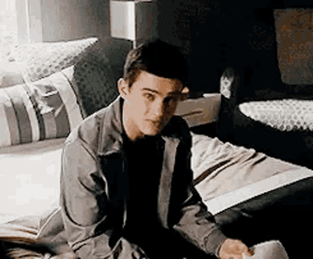 a young man is sitting on a bed in a bedroom looking at something .