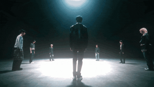 a man in a black jacket stands in the middle of a group of people in a dark room