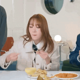 a woman is sitting at a table eating food with a fork and spoon .