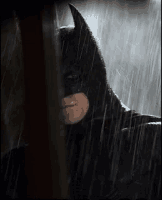 a close up of a man in a batman costume in the rain