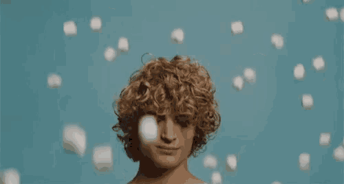 a man with curly hair is surrounded by marshmallows falling on him