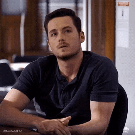 a man is sitting at a table with his hands folded in front of him .