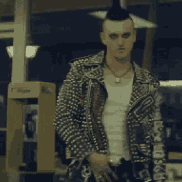 a man with a mohawk and a studded jacket is standing in front of a phone booth