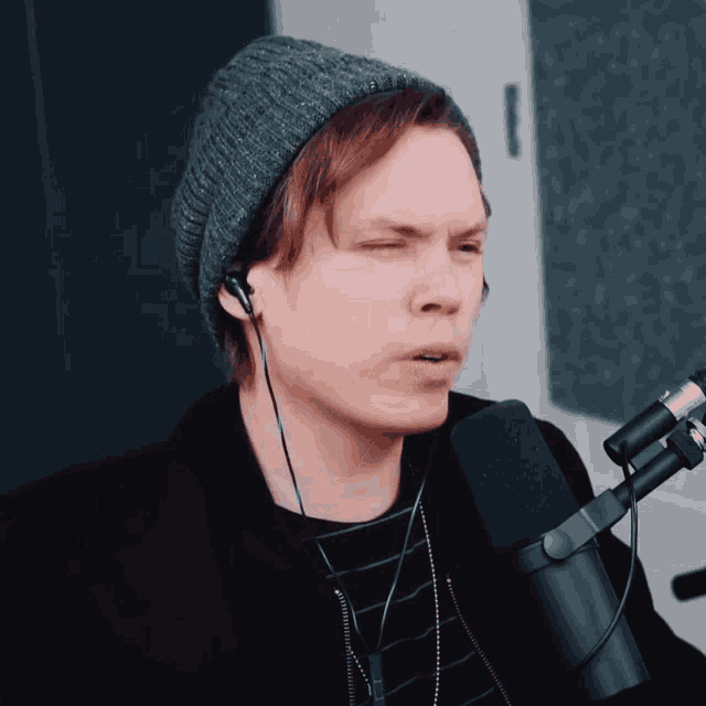 a man wearing a beanie and ear buds sings into a microphone
