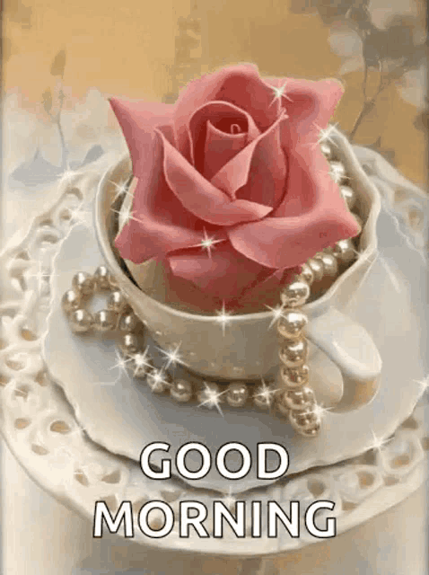 a cup of coffee with a pink rose and pearls on a saucer with the words `` good morning '' .