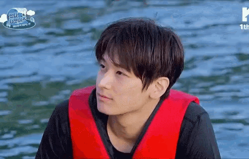 a young man wearing a red life jacket is sitting in the water .