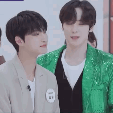 two young men are standing next to each other in a room . one is wearing a green sequined jacket .