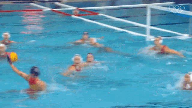 a group of people are swimming in a pool with the olympic rings on the wall