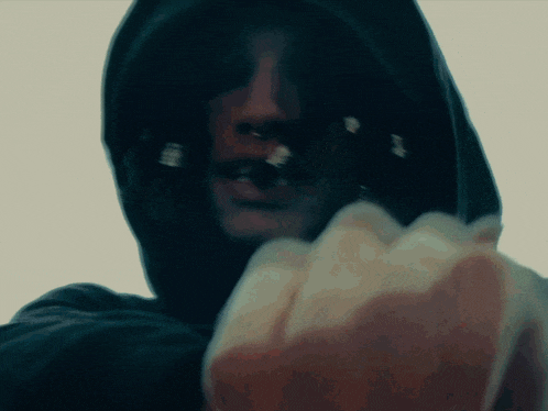 a man in a hooded sweatshirt holds his fist up towards the camera