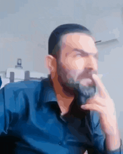 a man with a beard is wearing a blue shirt and covering his mouth with his hand