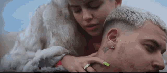 a woman in a fur coat is touching a man 's neck with a green nail polish