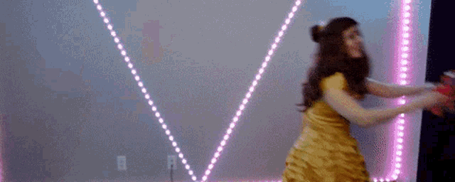 a woman in a yellow dress is holding a stuffed animal in front of a wall with lights .
