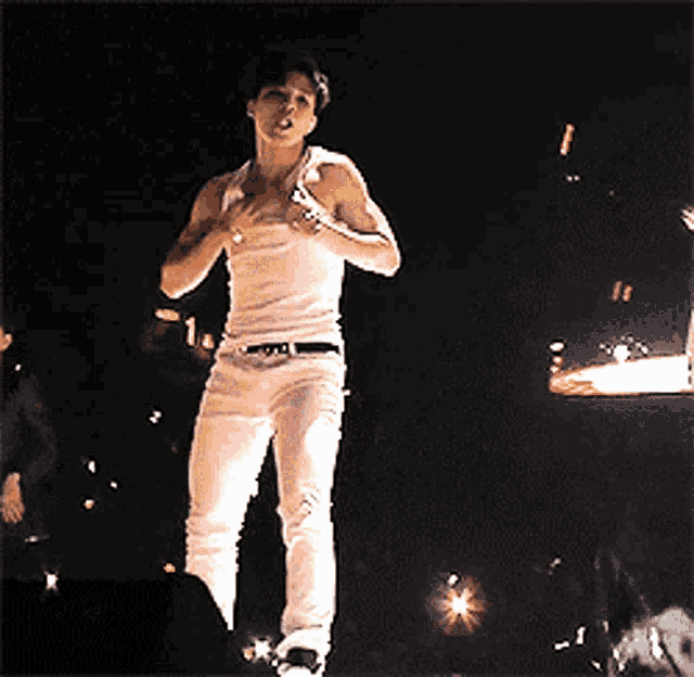 a man in a white shirt and white pants is standing in the dark .