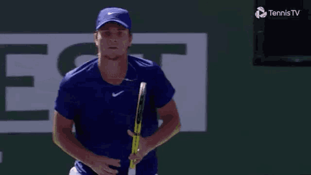 a man in a blue shirt is holding a tennis racquet in his hand .