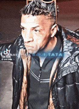 a man wearing sunglasses and a black jacket has a tiktok watermark on his jacket