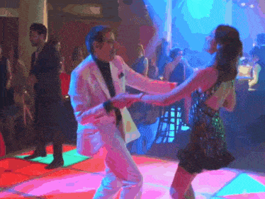 a man in a suit is dancing with a woman in a dress on a dance floor