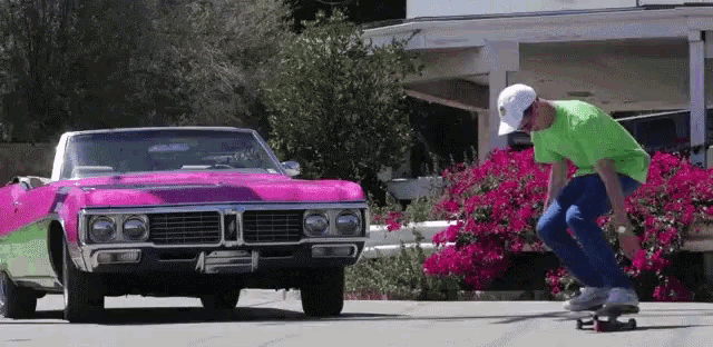 a man in a green shirt is riding a skateboard in front of a pink car