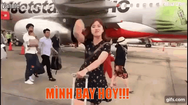 a woman is standing in front of a jetstar plane holding a suitcase .
