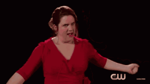 a woman in a red dress is standing with her arms outstretched and a cw logo in the background .