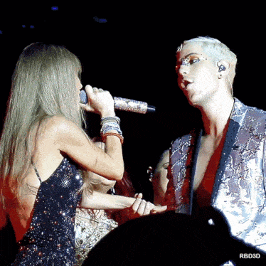 a woman singing into a microphone next to a man in a suit with a rbd3d watermark