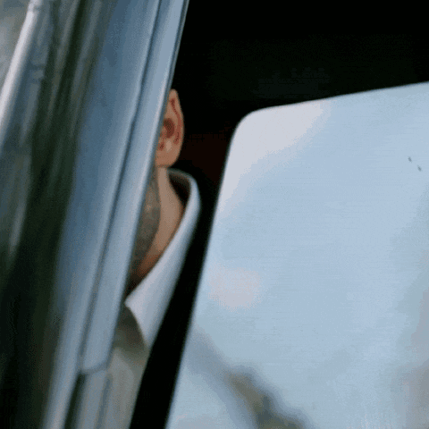 a man in a suit and white shirt is looking out of a car window .