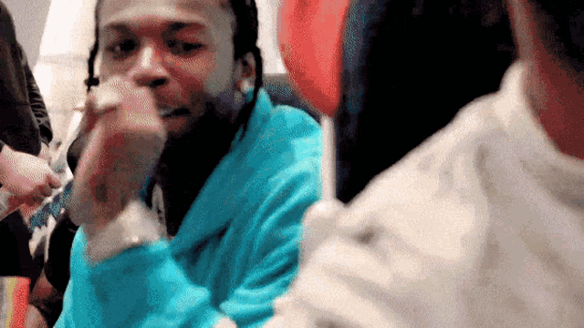a man in a blue sweatshirt is smoking a cigarette while sitting in a crowd of people .