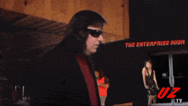 a man wearing sunglasses is standing in front of a sign that says the enterprise room