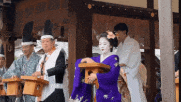 a woman in a purple kimono is carrying a wooden box in a temple