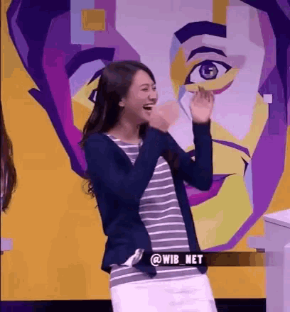 a woman is laughing in front of a colorful painting of a man 's face .
