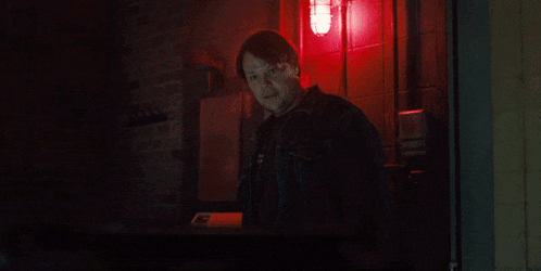 a man in a denim jacket stands in front of a red light that says " emergency "