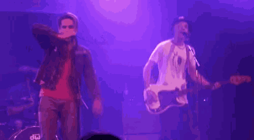 a man singing into a microphone while another man plays a guitar in front of a drum set that says dw on it