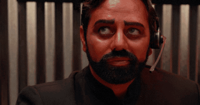 a man with a beard wearing a headset looks at the camera