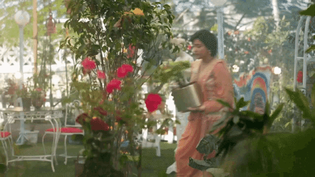 a woman is watering flowers in a greenhouse with a bucket