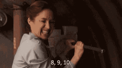 a woman is laughing while holding a barbell in a dark room and smiling .