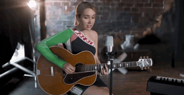 a woman is playing a guitar in front of a microphone and has a green sleeve that says bitch on it