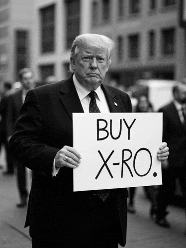 a man in a suit and tie holds a sign that says buy x-ro