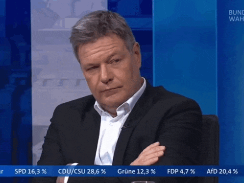 a man in a suit is sitting in front of a bulletin board that says bundeswahl