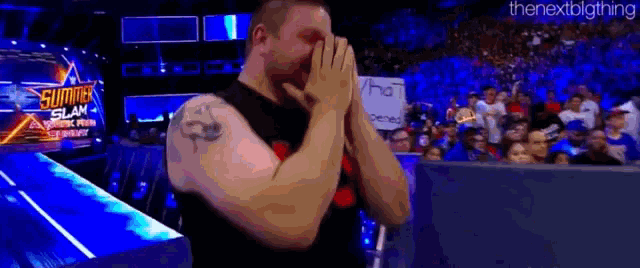 a man is covering his face with his hands while standing in front of a crowd at a wrestling match .
