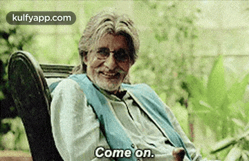 a man with glasses and a beard is sitting in a chair and saying `` come on '' .