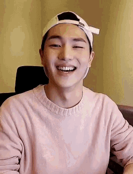 a young man wearing a baseball cap and a pink sweater smiles for the camera
