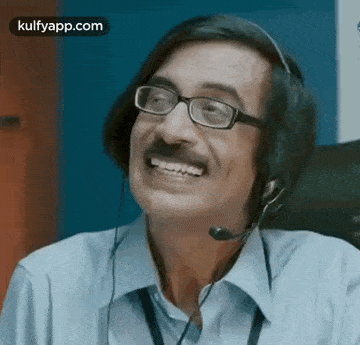 a man wearing glasses and a headset is smiling while talking on a phone .